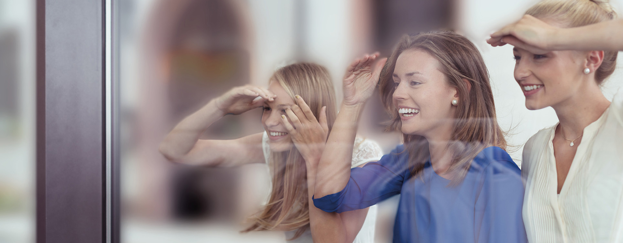 Drei Frauen schauen neugierig durchs Schaufenster in einen Laden